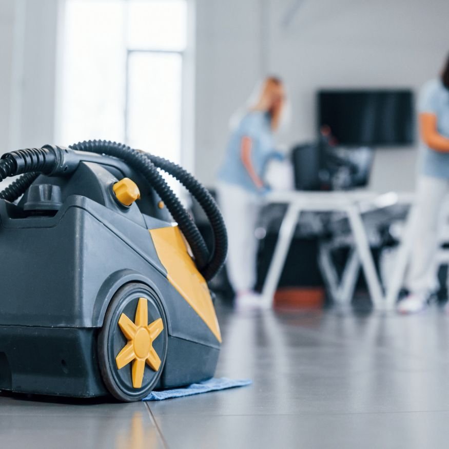 Woman uses vacuum cleaner. Group of workers clean modern office together at daytime.